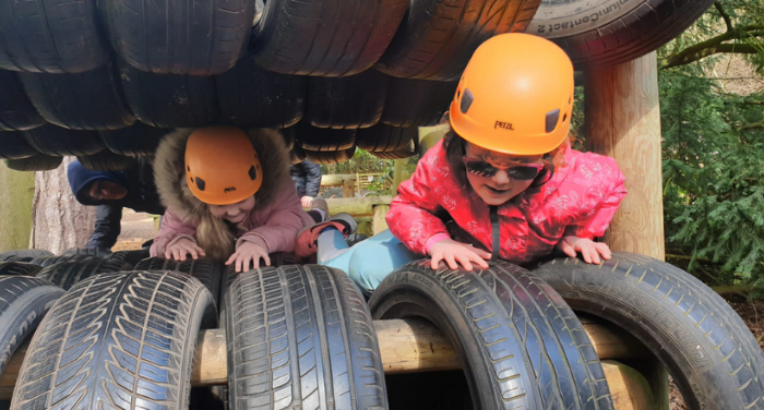 Two girls wearing helmets crawl through a tunnel of tires as part of an obstacle course