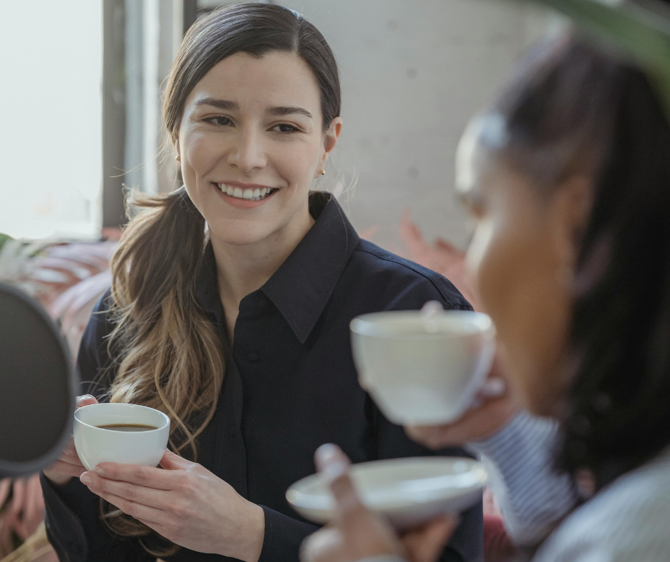 A woman holding a cup of tea smiling at another woman in the forground.